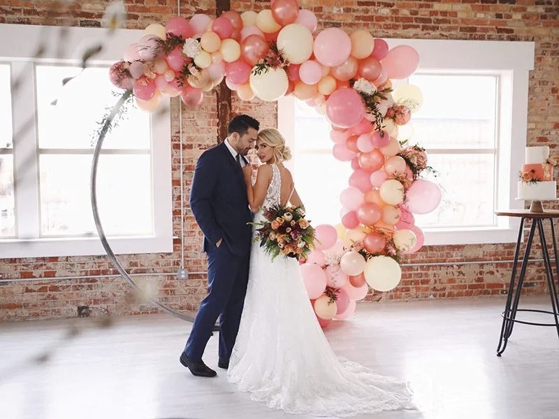 Pink and peach organic balloon hoop backdrop for a wedding couple