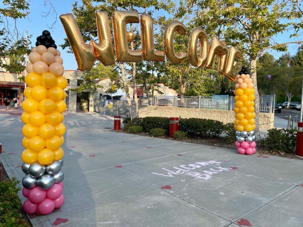 Yellow, silver, and pink pencil-style balloon columns with gold Welcome foil letters