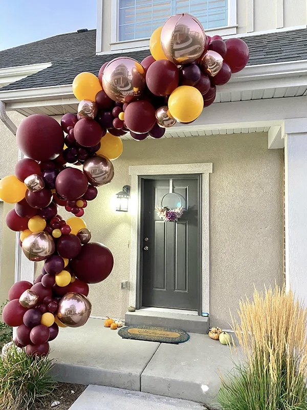 Burgundy, gold, and yellow organic balloon garland over a front door