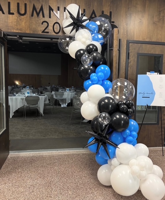 Blue, black, white, and clear balloon garland framing an Alumni Hall doorway